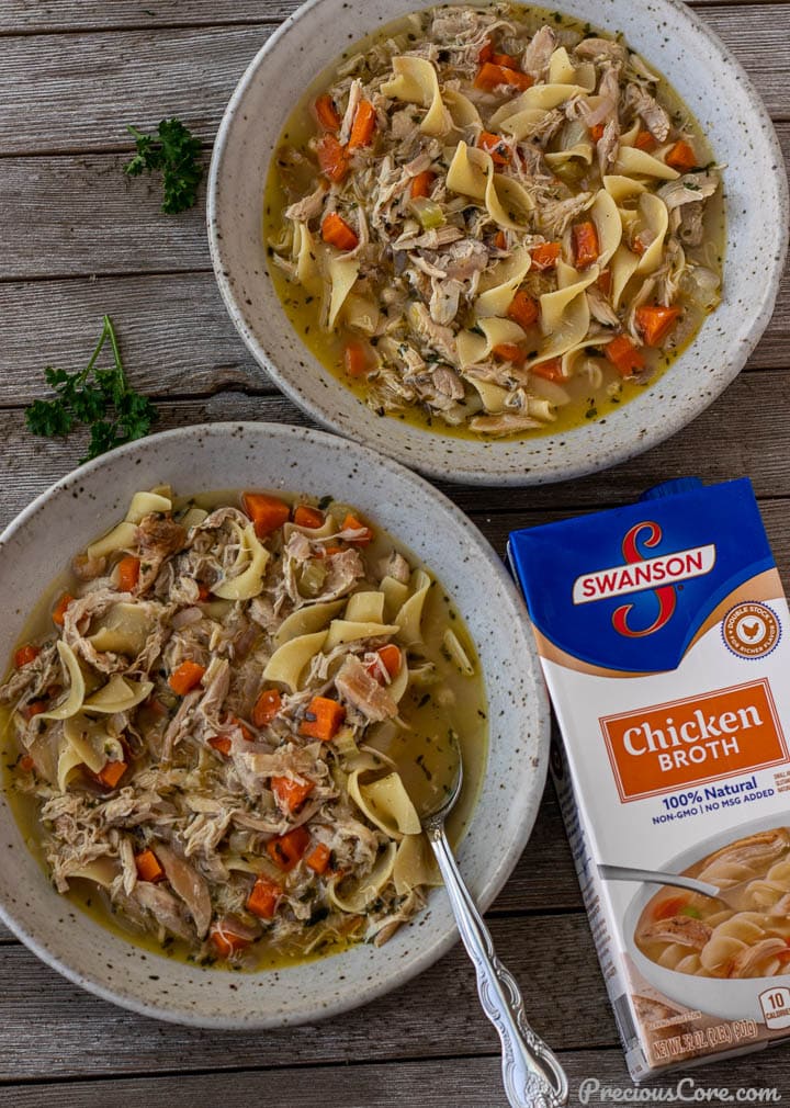 2 bowls of chicken noodle soup with a box of chicken broth on the side.