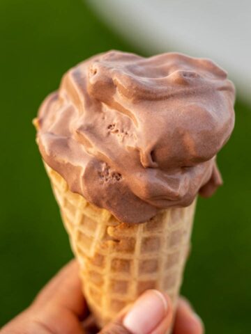 HAND HOLDING CONE OF CHOCOLATE ICE CREAM