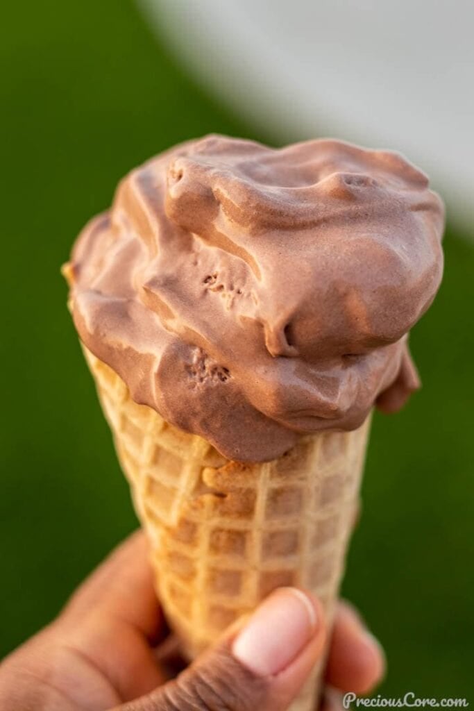 HAND HOLDING CONE OF CHOCOLATE ICE CREAM