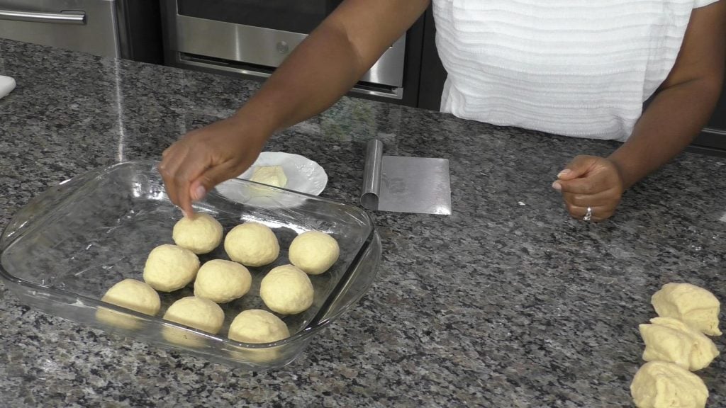 Hand placing balls of dough into a baking dish