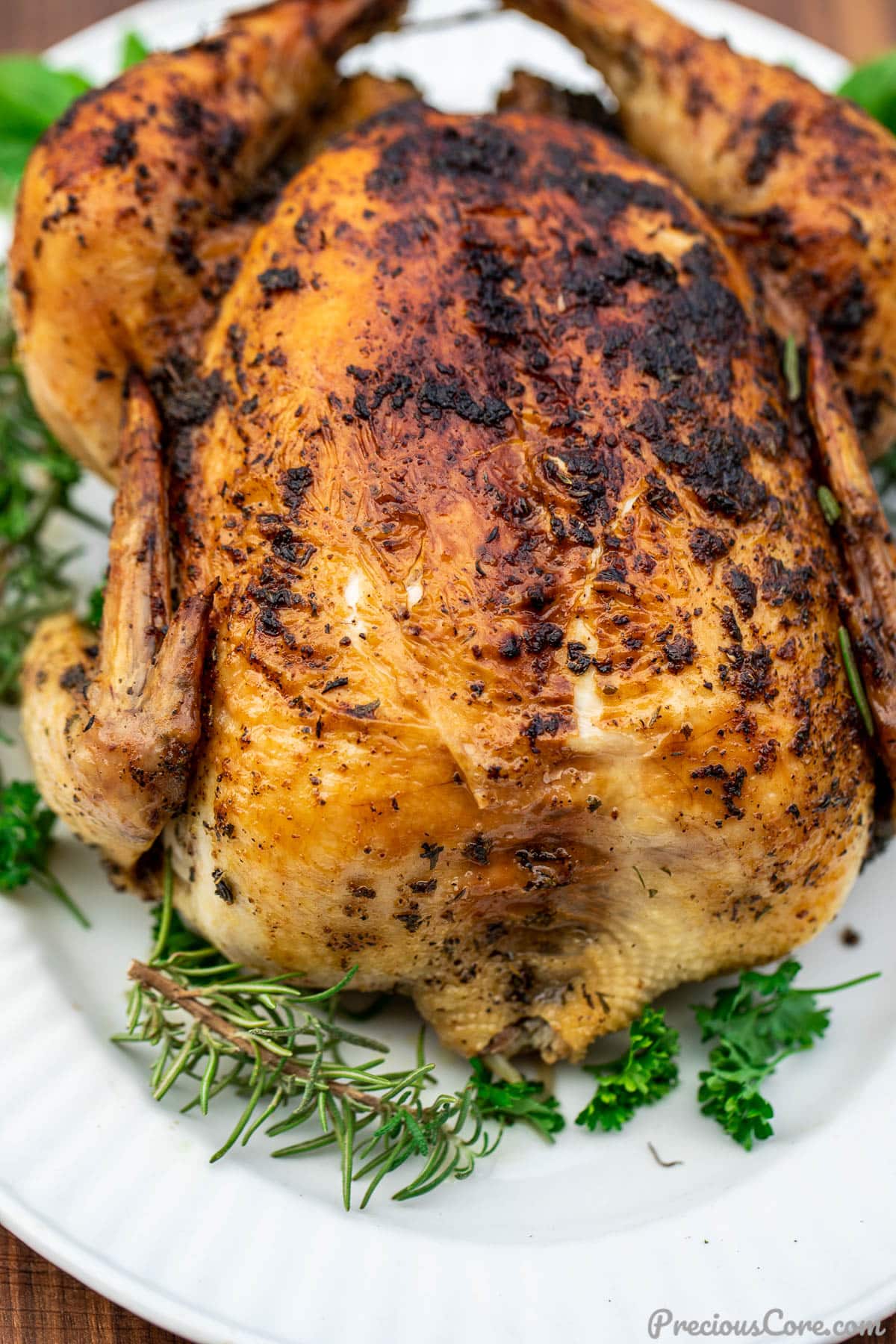 Whole herb roasted chicken on a platter, garnished with fresh herbs.