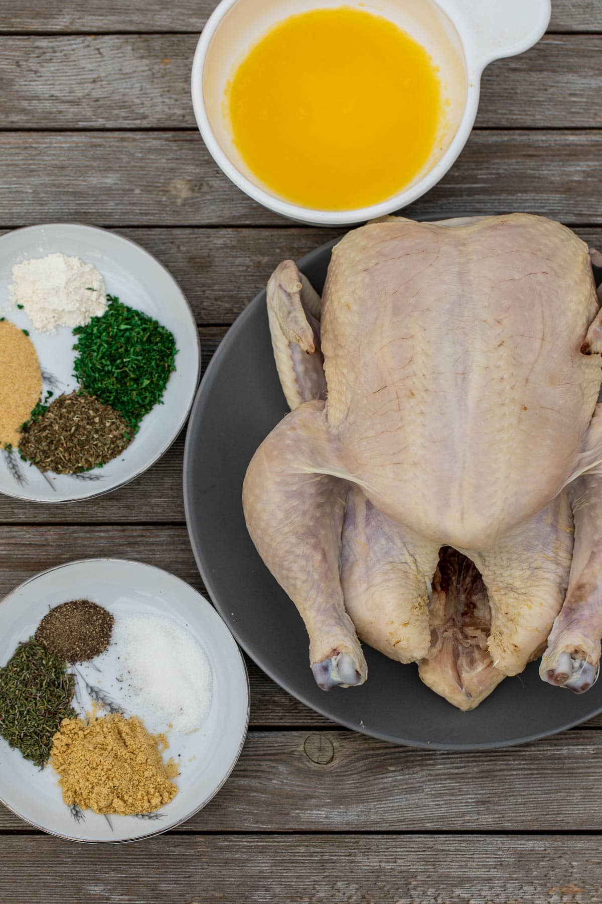 A whole chicken, spices and seasoning laid out on a wooden board.