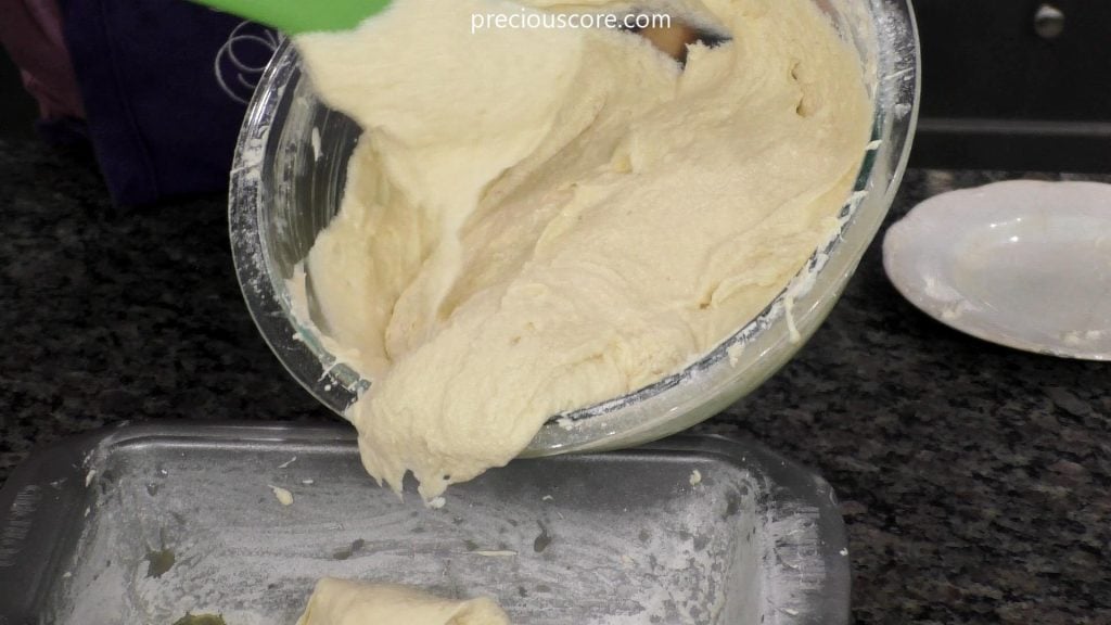 Process shot of hand pouring batter into a greased loaf pan