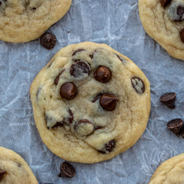 Chocolate chip cookies on parchment paper with chocolate sprinkles lying around.