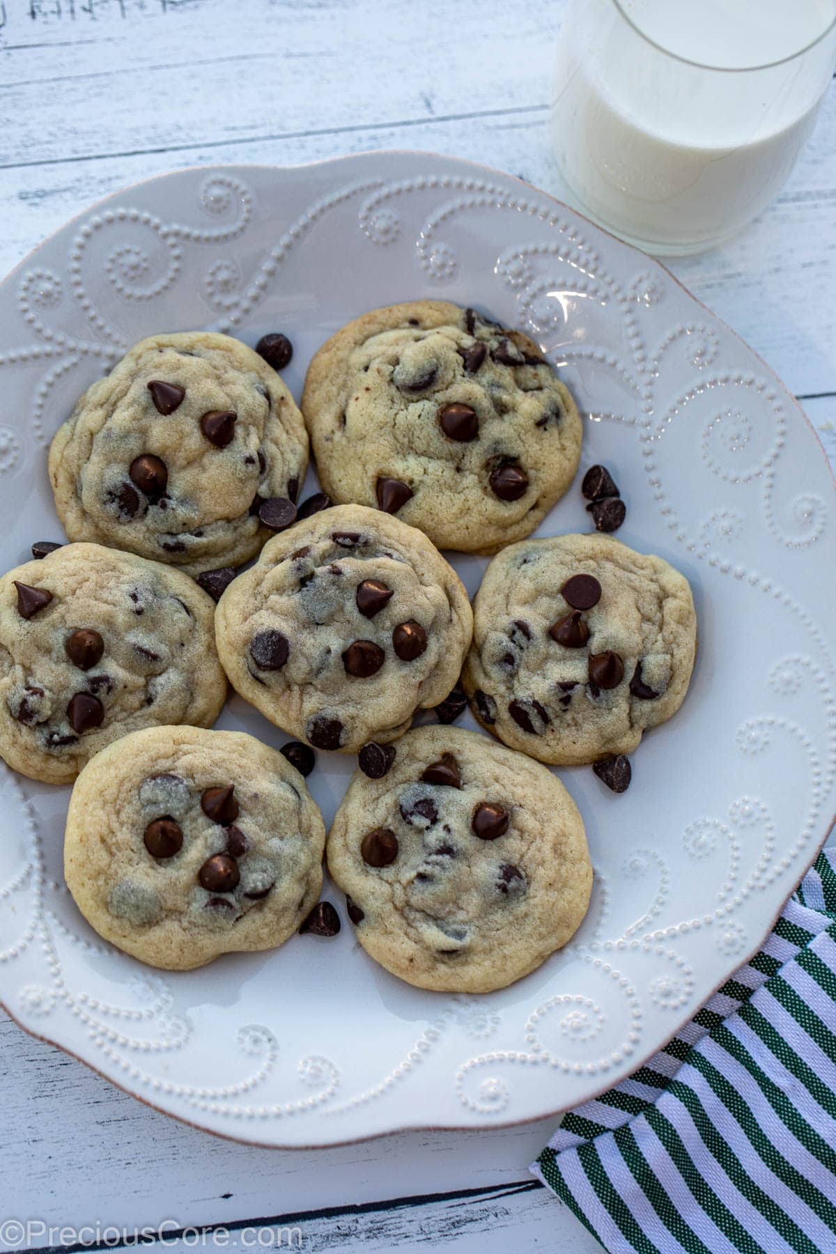 A plate of chocolate chip cookies, a dish cloth nearby and a glass of milk.