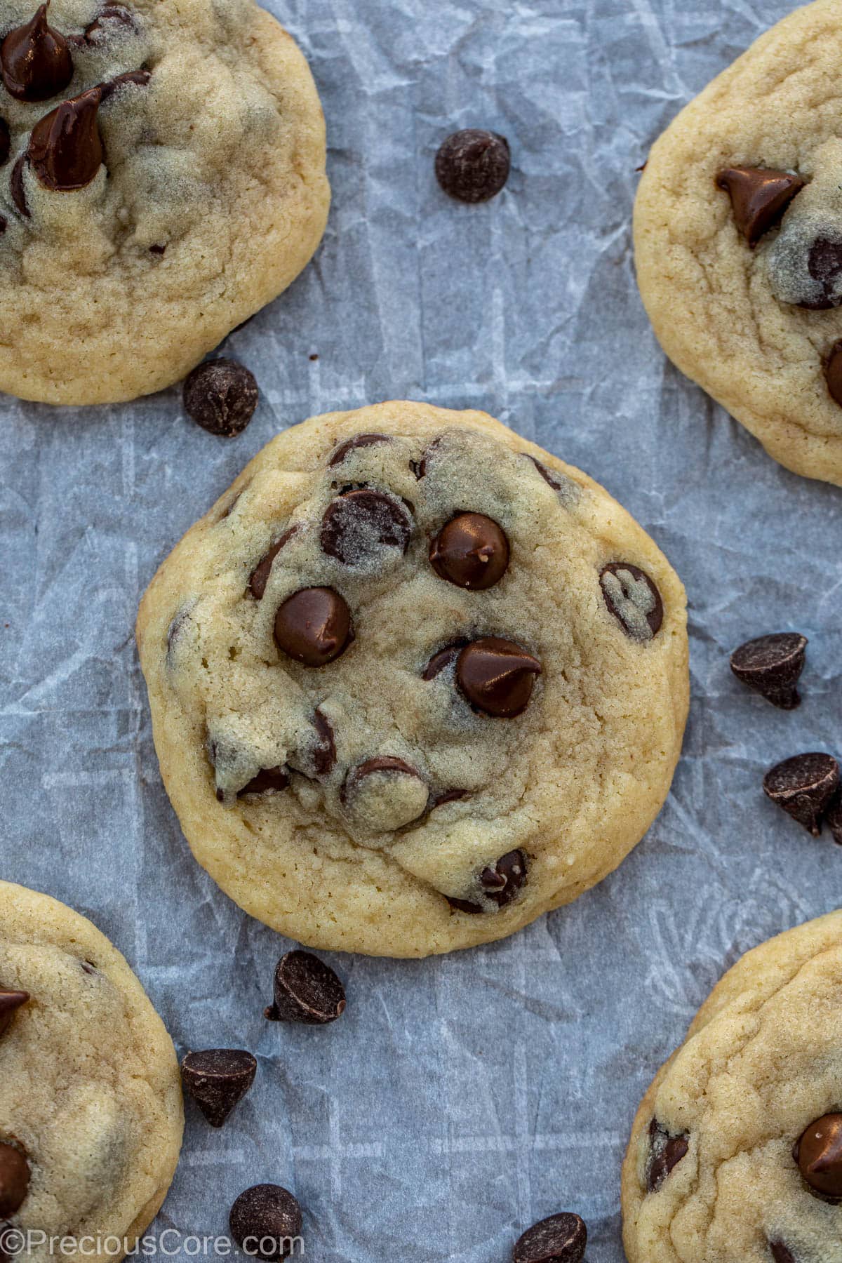 Chocolate chip cookies on parchment paper with chocolate sprinkles lying around.