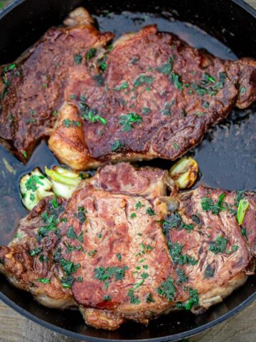 2 cooked ribeye steaks in a cast iron pan