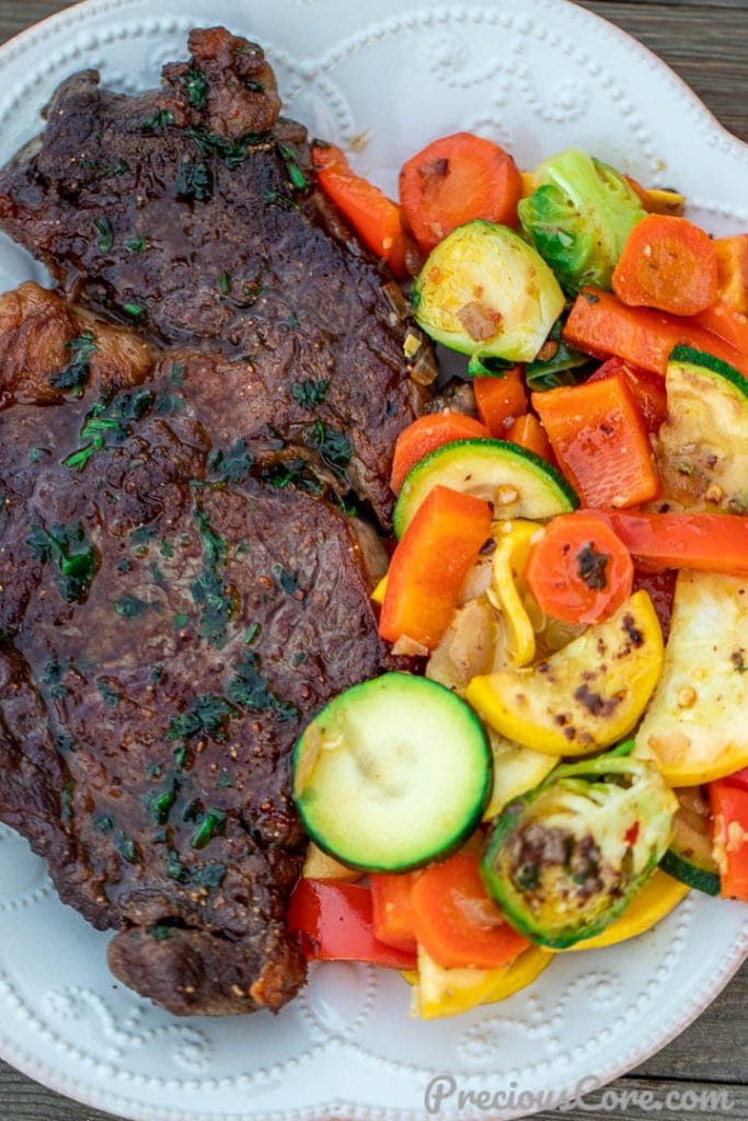 Pan seared steak and sautéed veggies on a white plate.