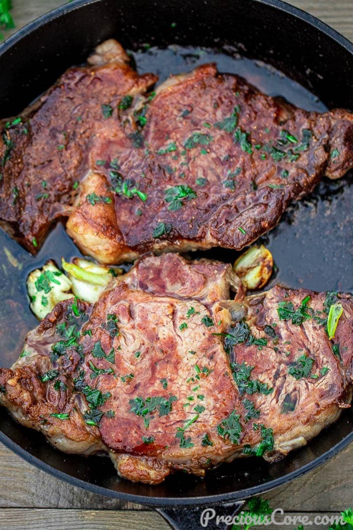 2 cooked ribeye steaks in a cast iron pan