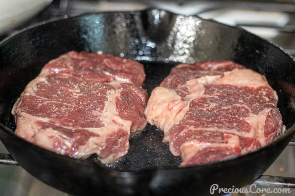 Raw ribeye steak in a cast iron skillet.