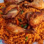 Jollof Rice on a serving platter with cooked chicken thighs and drumsticks on top