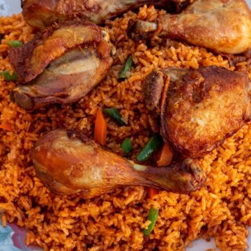 Jollof Rice on a serving platter with cooked chicken thighs and drumsticks on top