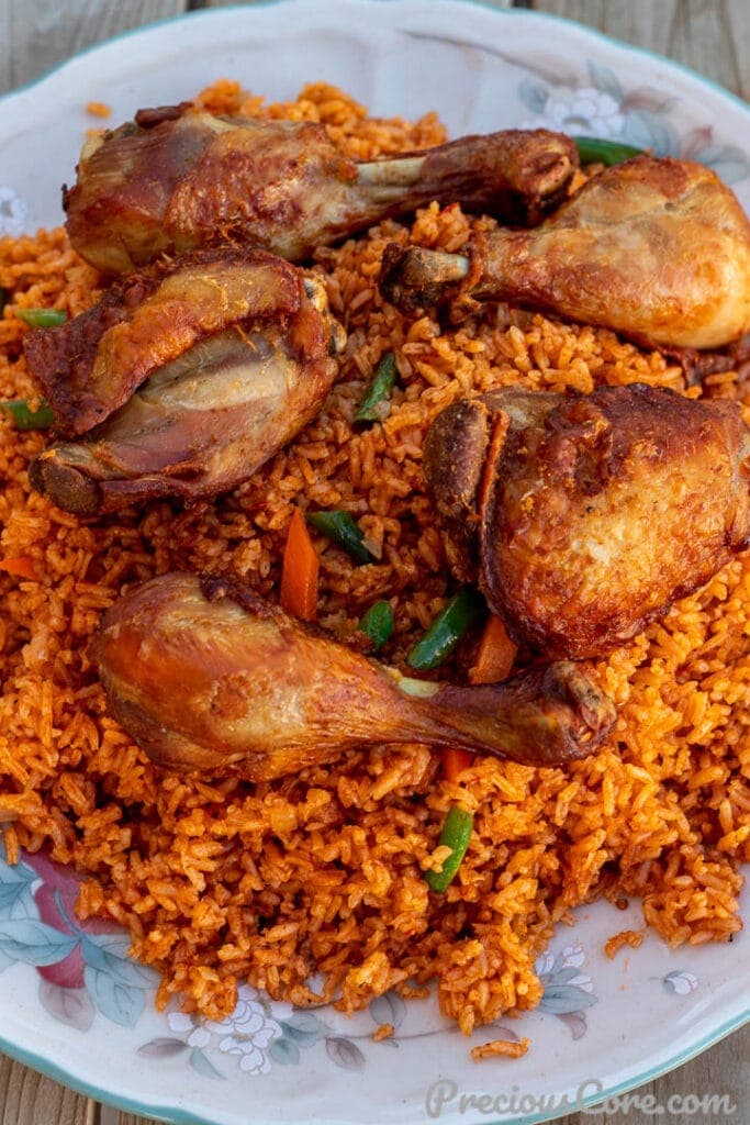 Jollof Rice on a serving platter with cooked chicken thighs and drumsticks on top