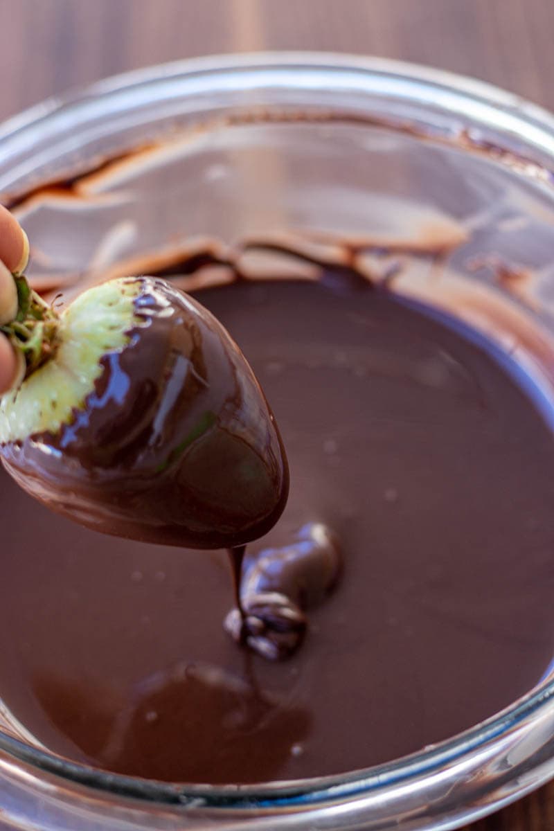 hand holding a strawberry dipped in melted chocolate.