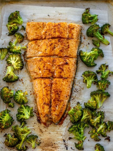 Large salmon fillet and roasted broccoli on a sheet pan