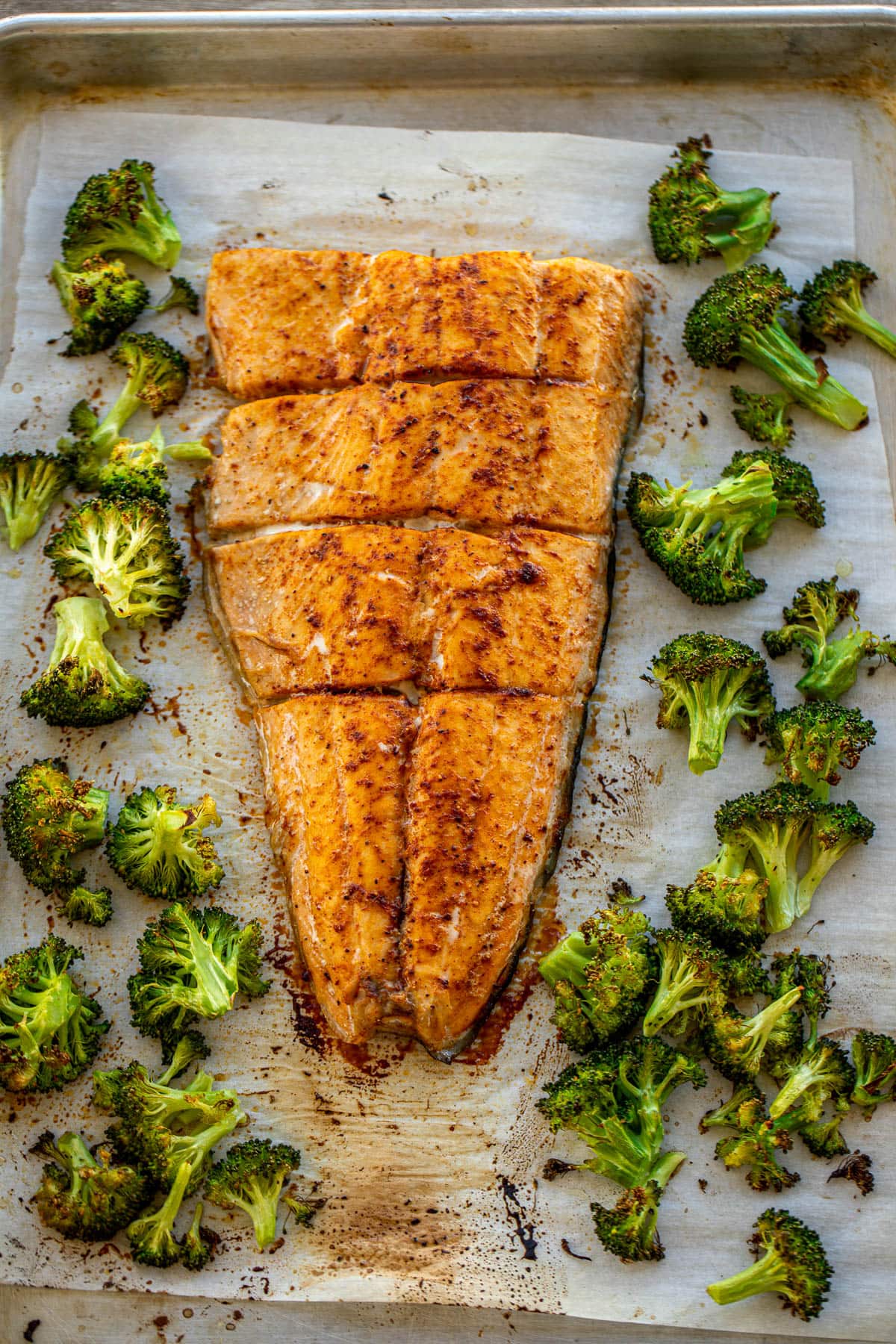 Large salmon fillet and roasted broccoli on a sheet pan