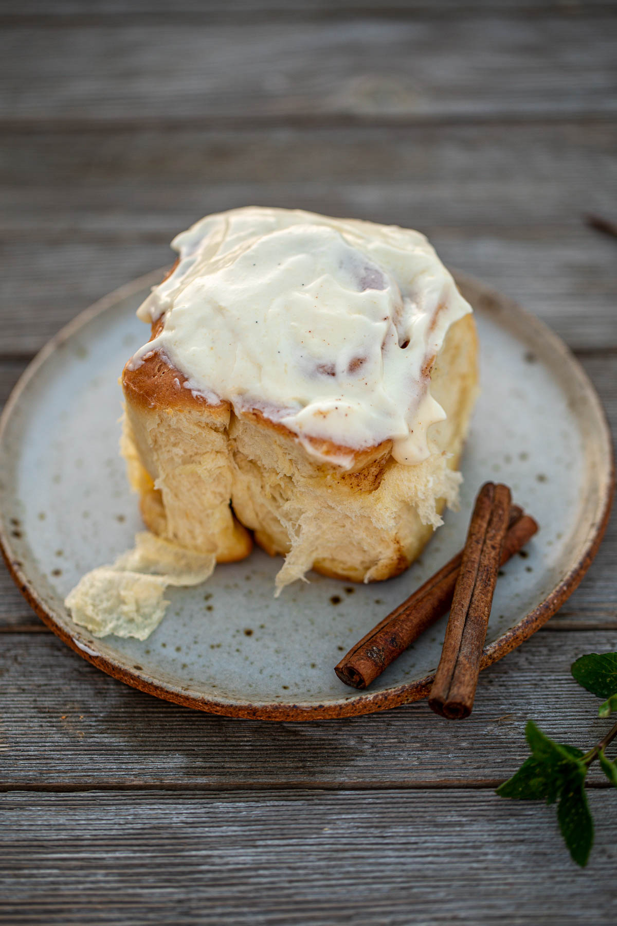 A cinnamon roll on a plate, topped with cream cheese frosting.