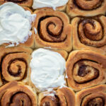 Cinnamon rolls in a pan, some of the rolls frosted with cream cheese frosting