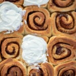 Cinnamon rolls in a pan, some of the rolls frosted with cream cheese frosting