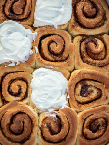 Cinnamon rolls in a pan, some of the rolls frosted with cream cheese frosting