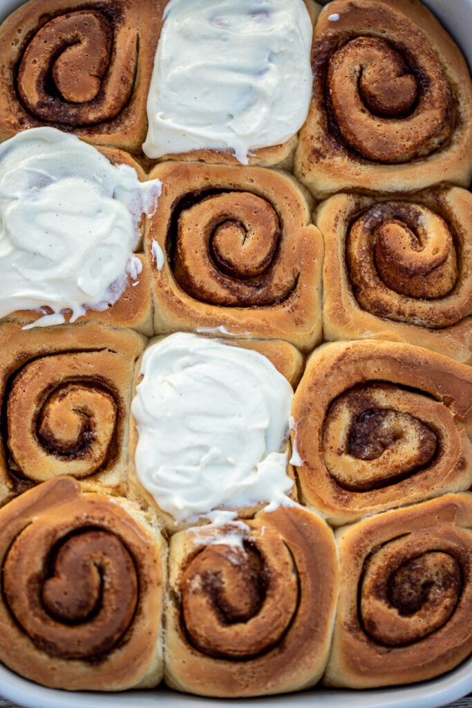 Cinnamon rolls in a pan, some of the rolls frosted with cream cheese frosting