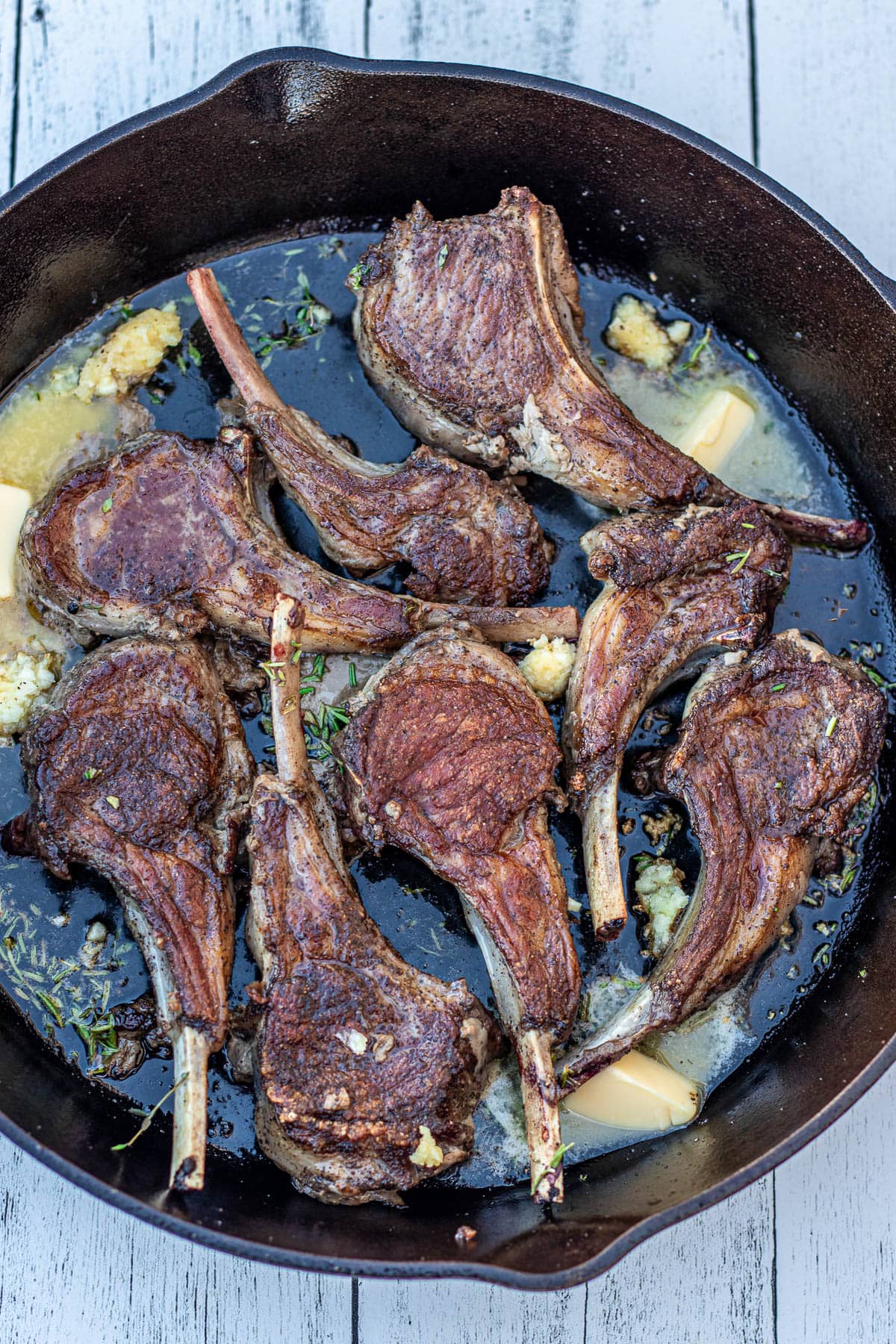 Flipped lamb chops with butter and garlic in pan.
