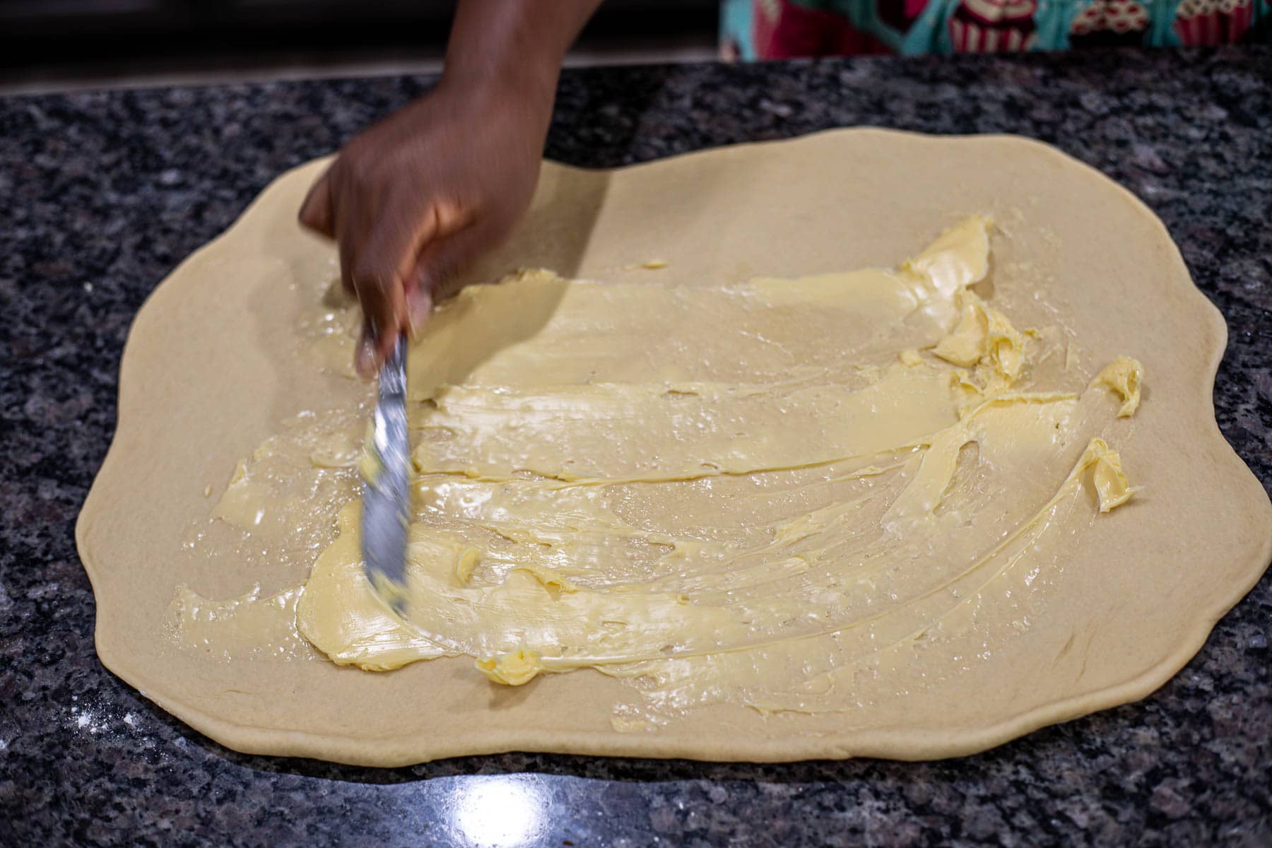 hand spreading butter on rolled out dough