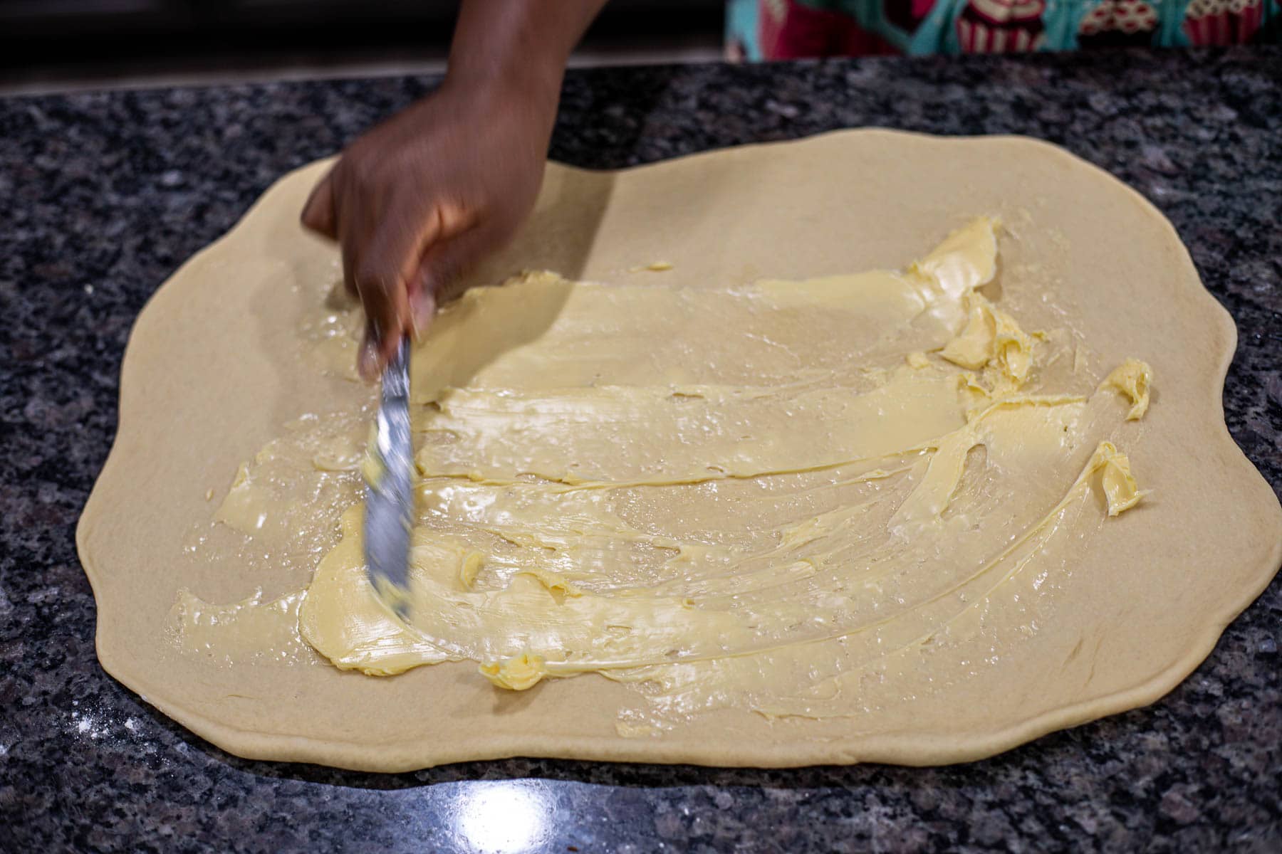 Hand spreading softened butter on rolled out dough.