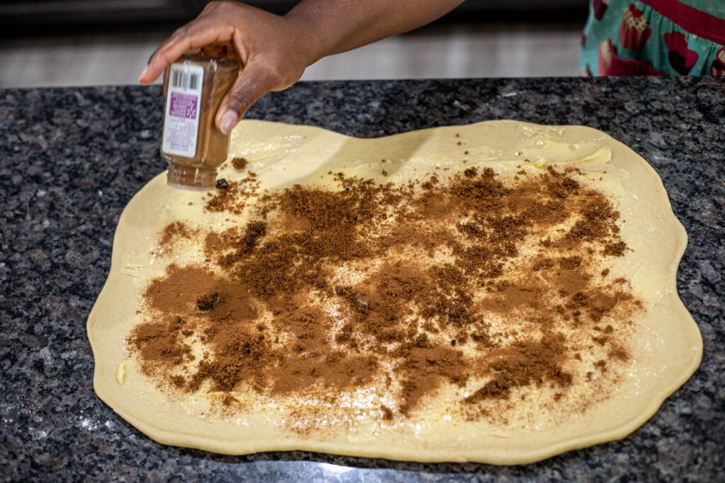 Hand sprinkling ground cinnamon over dough