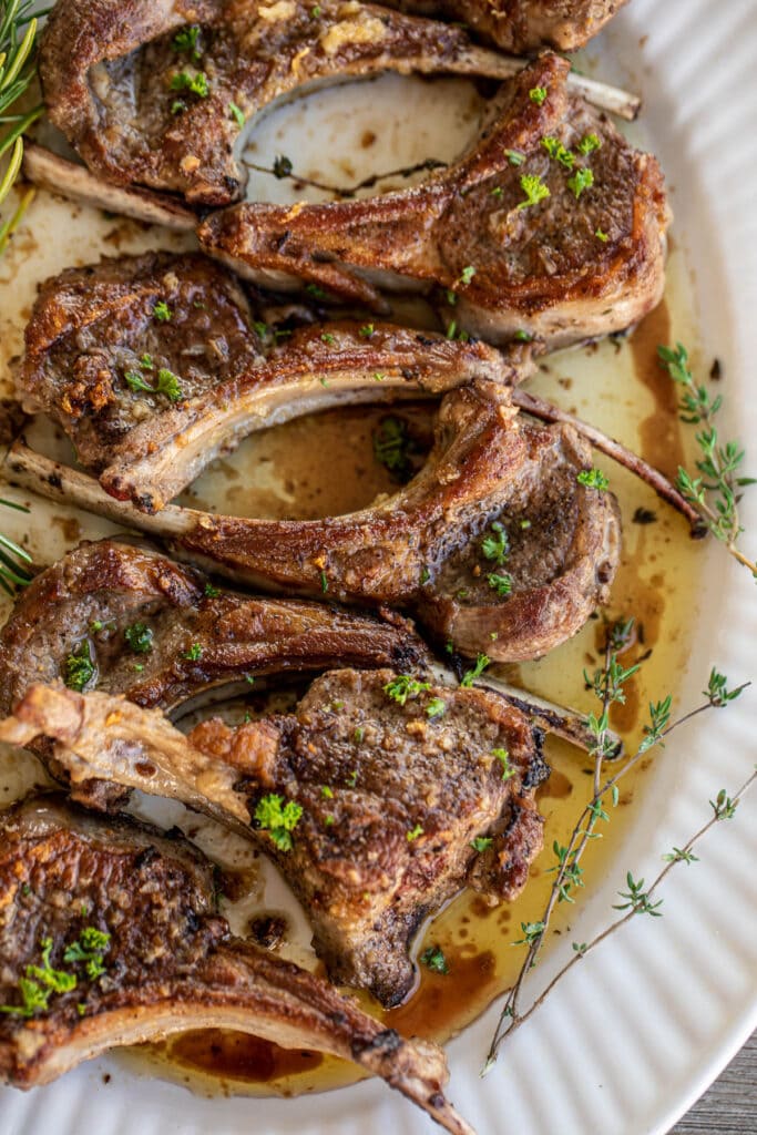 Pan seared lamb chops served on a large tray, garnished with fresh thyme and rosemary leaves