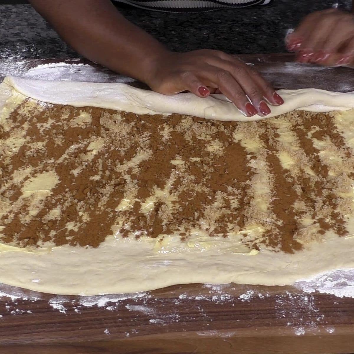 Hand rolling cinnamon roll dough into a log.