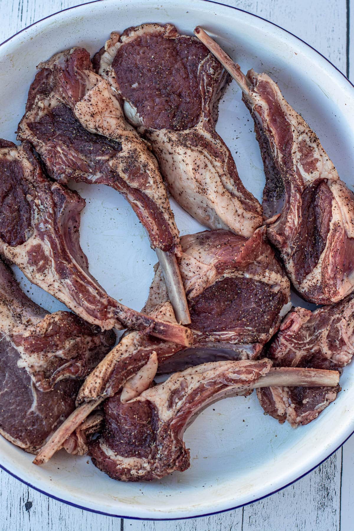 Seasoned lamb chops in a white bowl.