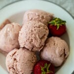 Scoops of ice cream on plate with fresh strawberry nearby