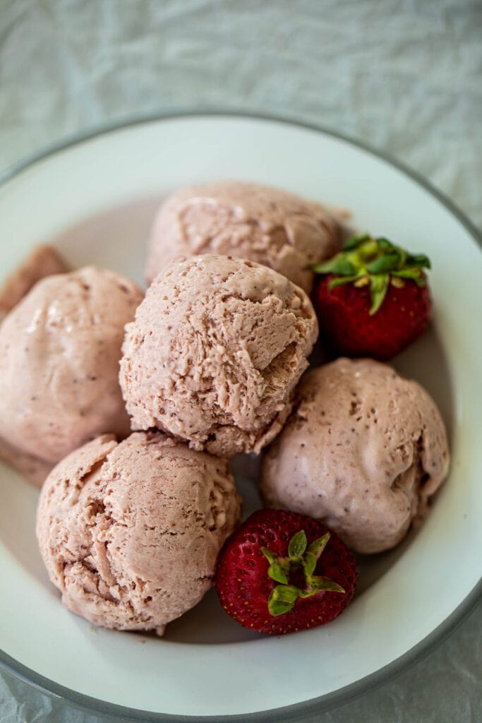 Scoops of ice cream on plate with fresh strawberry nearby