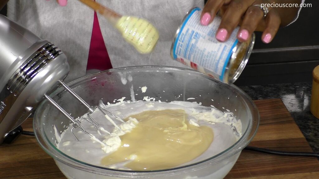 Sweetened condensed milk pouring from can into bowl.