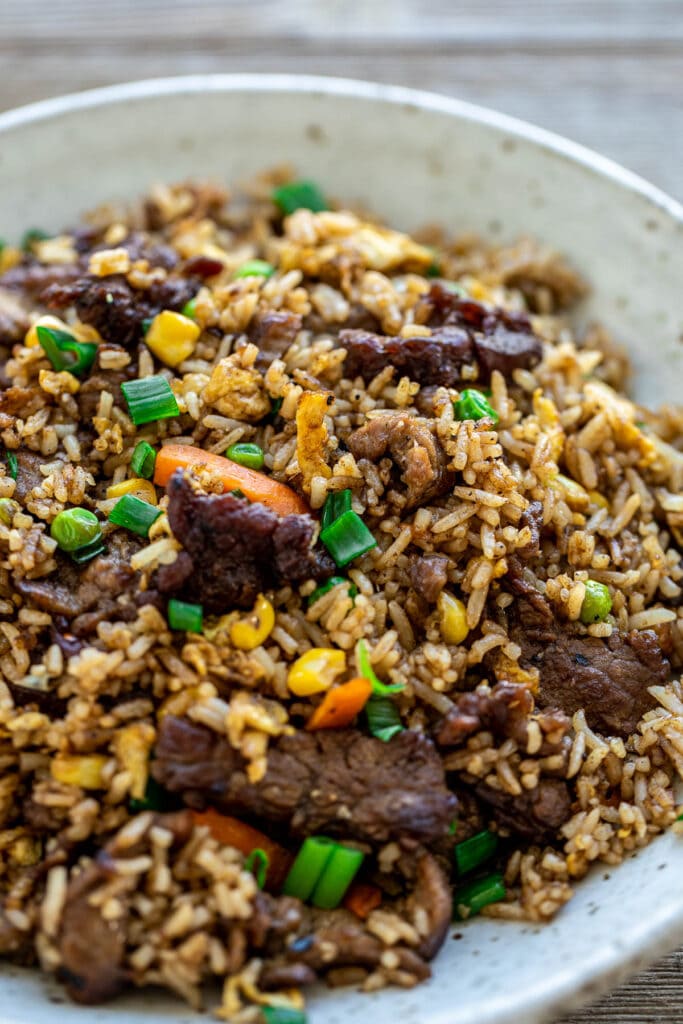 Fried rice in a bowl with veggies garnished with green onions.