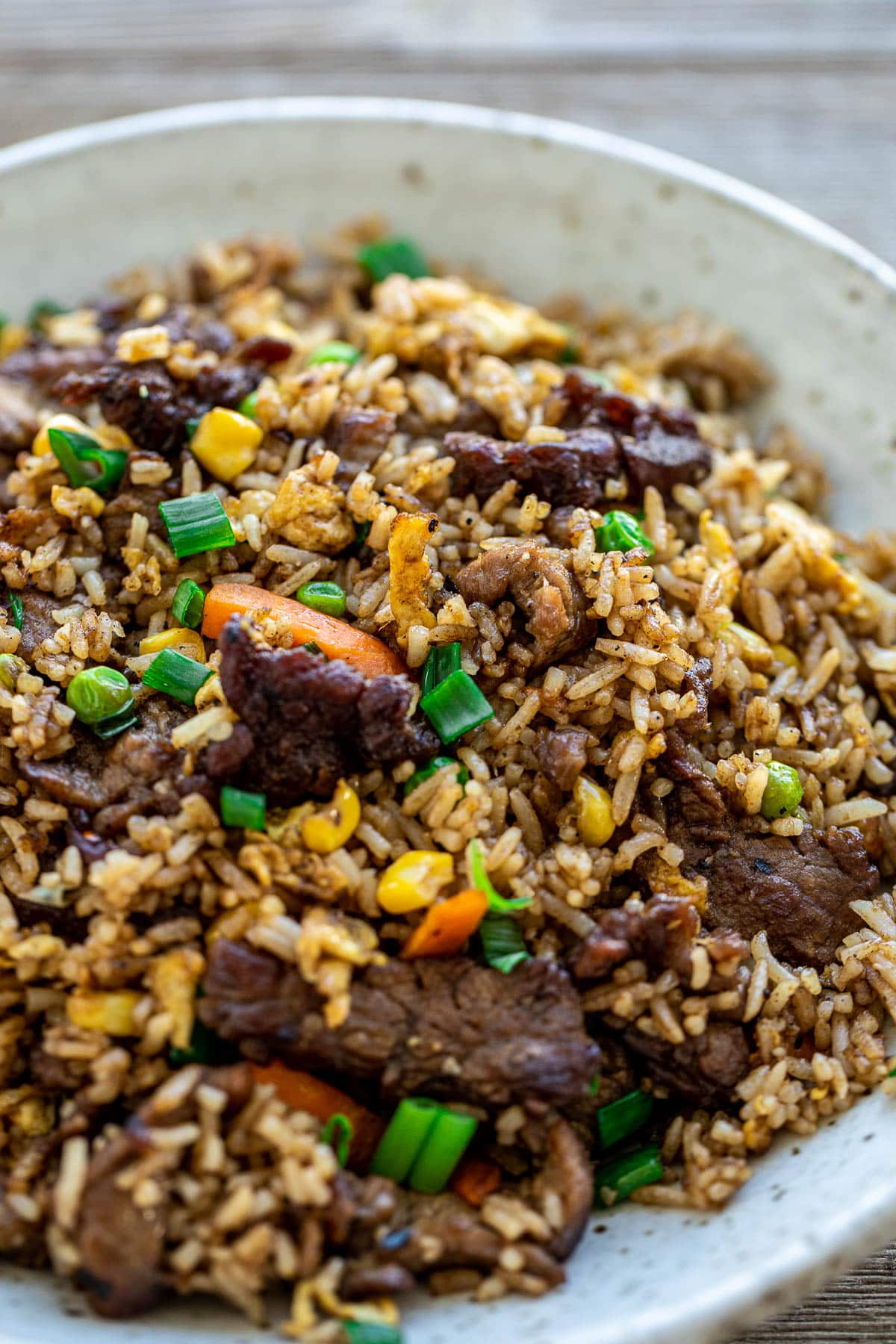 Fried rice in a bowl with veggies garnished with green onions.