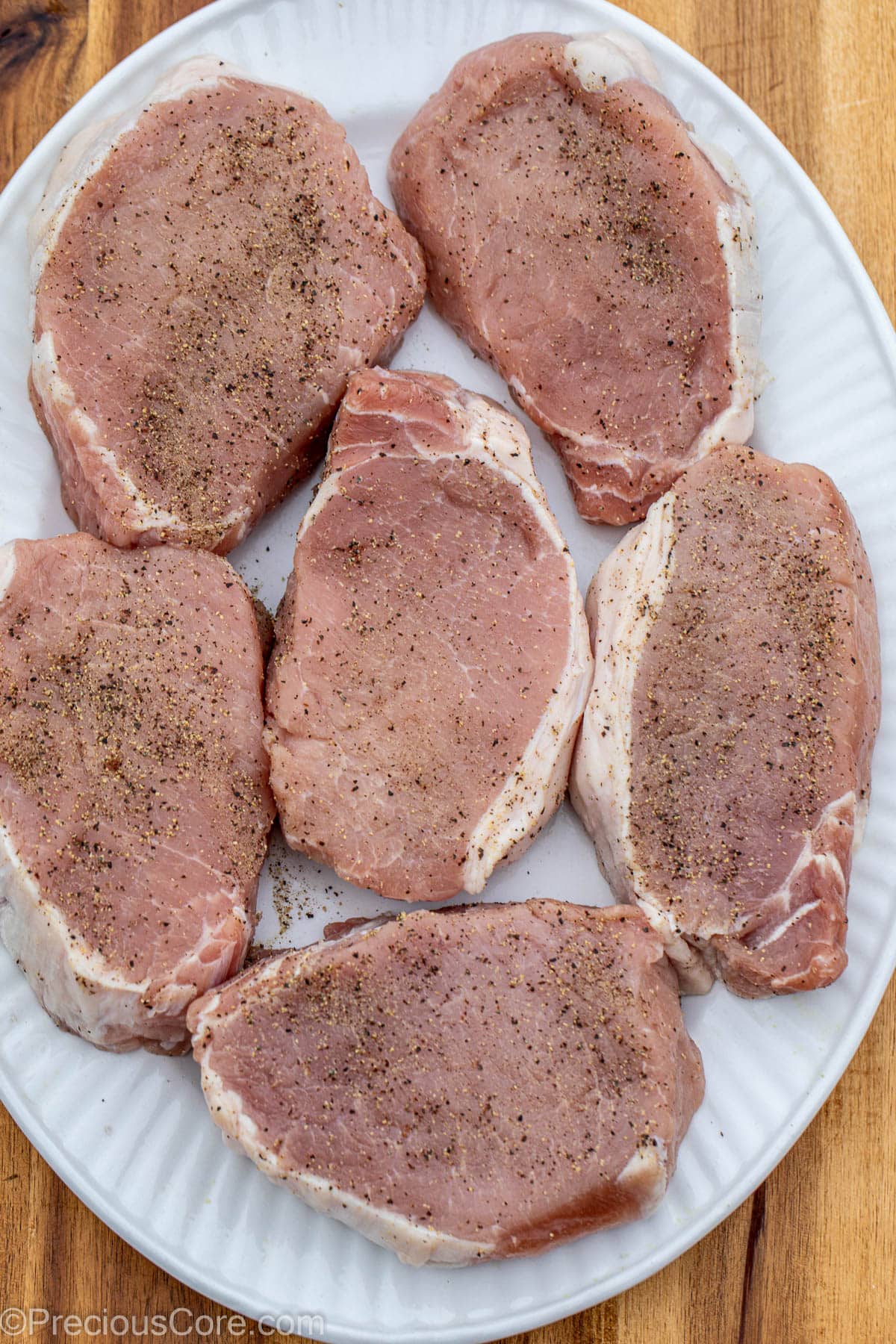 Pork chops in pan, seasoned with salt and pepper.