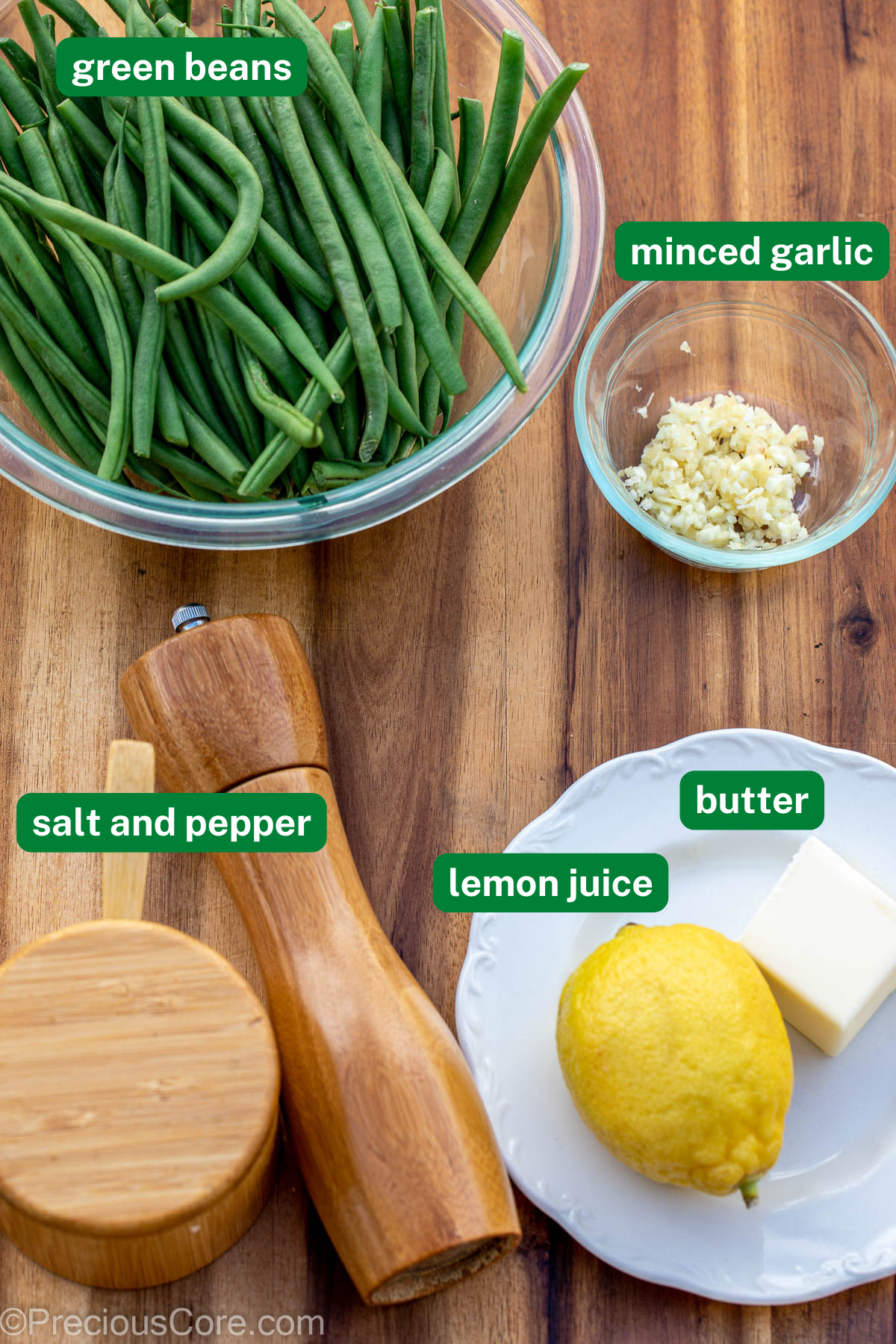 Fresh green beans, mined garlic, salt and pepper, lemon, and butter on chopping board.