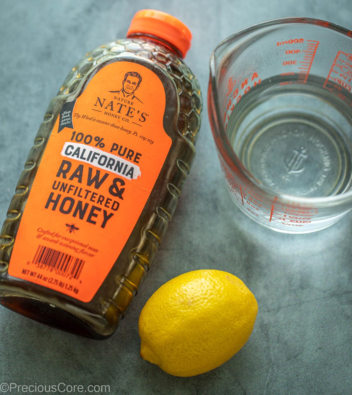 Container of honey, a lemon and water in a cup.