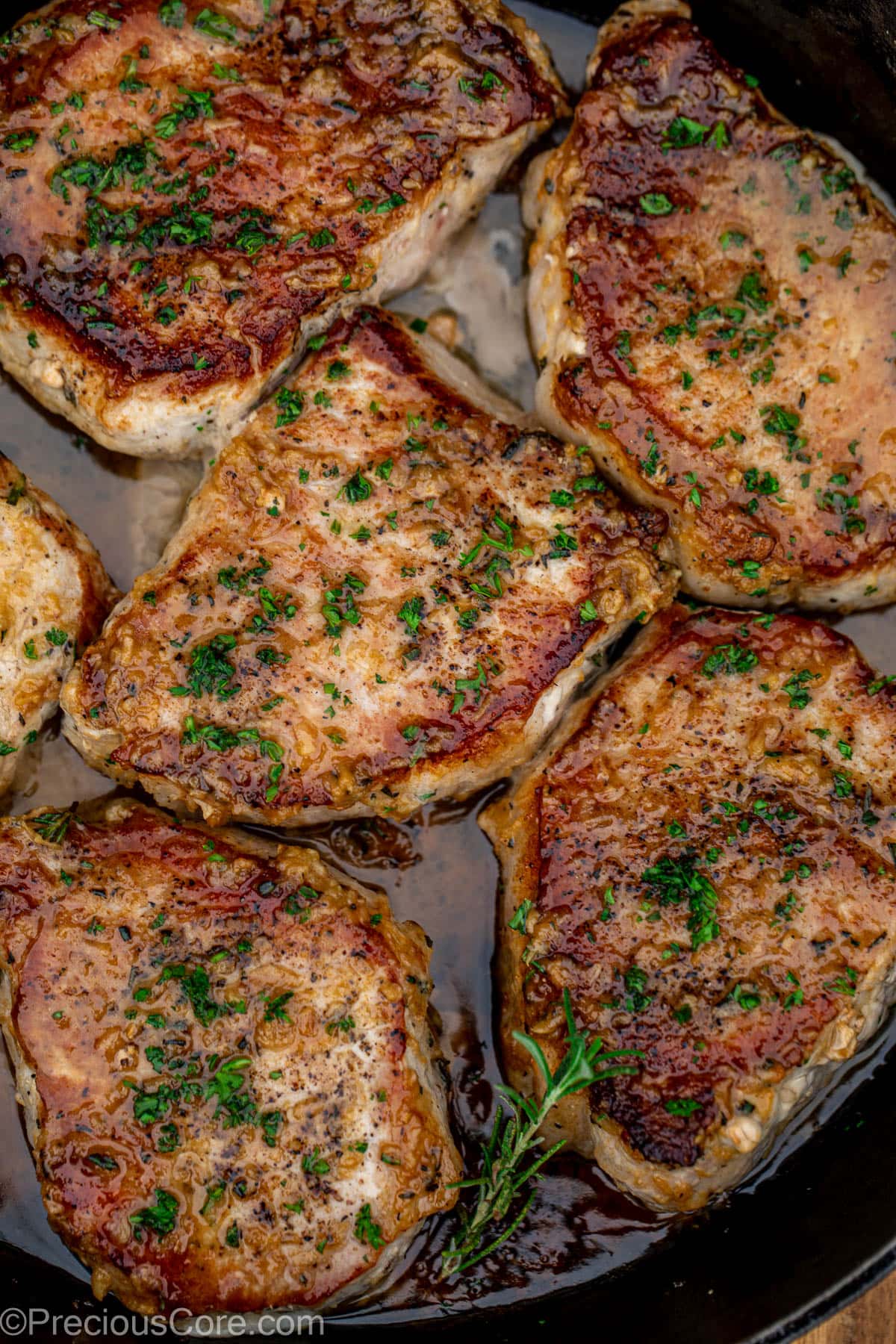 Pan seared boneless pork chops in a cast iron pan with butter underneath.