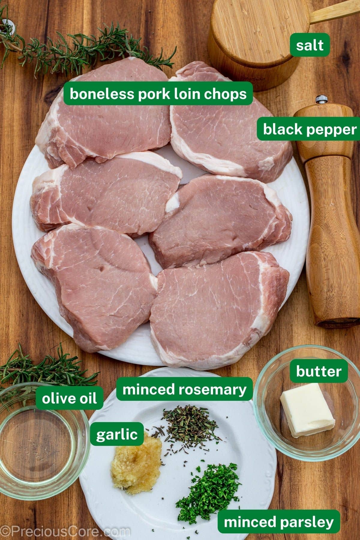 Ingredients for pork chops with labels over the ingredients. They include boneless pork chops, salt, pepper, olive oil, butter, garlic, and rosemary. 