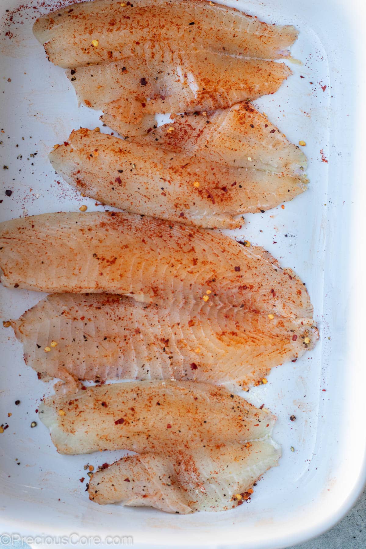 Seasoned tilapia fillets in a bowl.