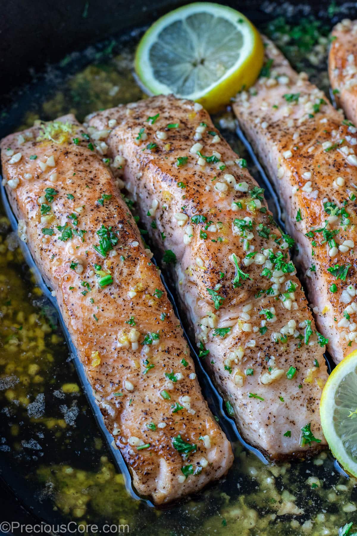 Lemon butter salmon in pan garnished with parsley and lemon slices.