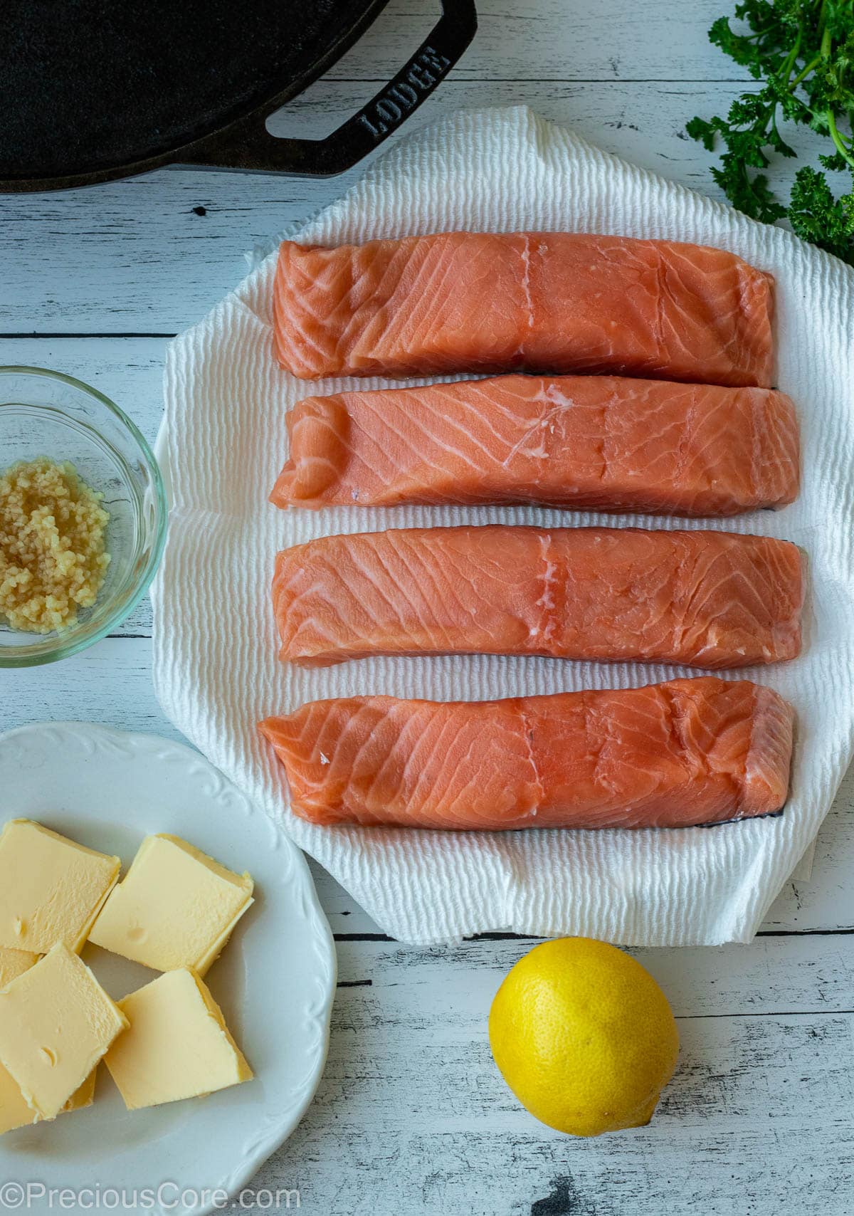 Raw salmon, minced garlic, butter, and lemon on a board.