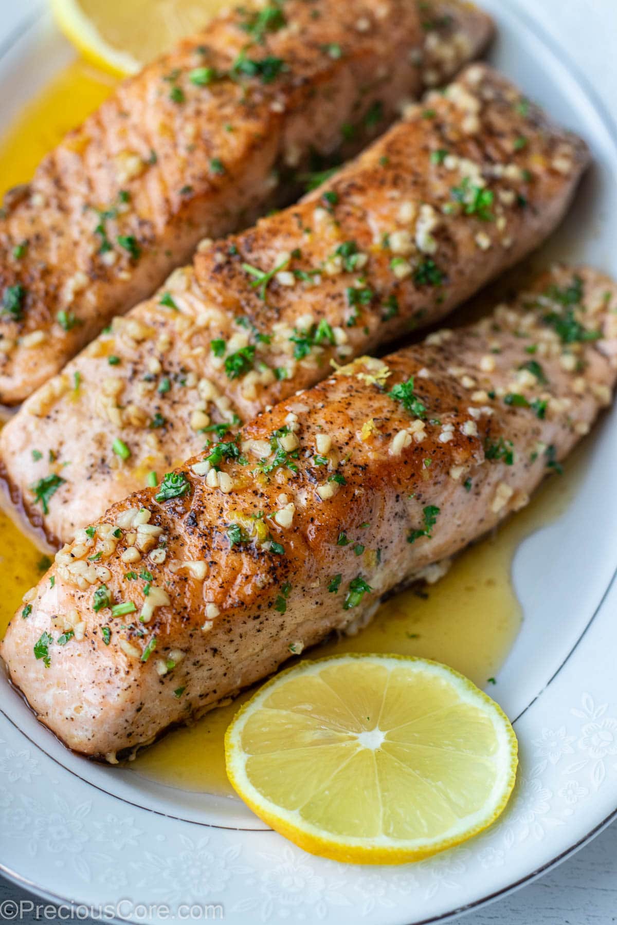 Cooked salmon fillets on a serving tray over lemon butter sauce.