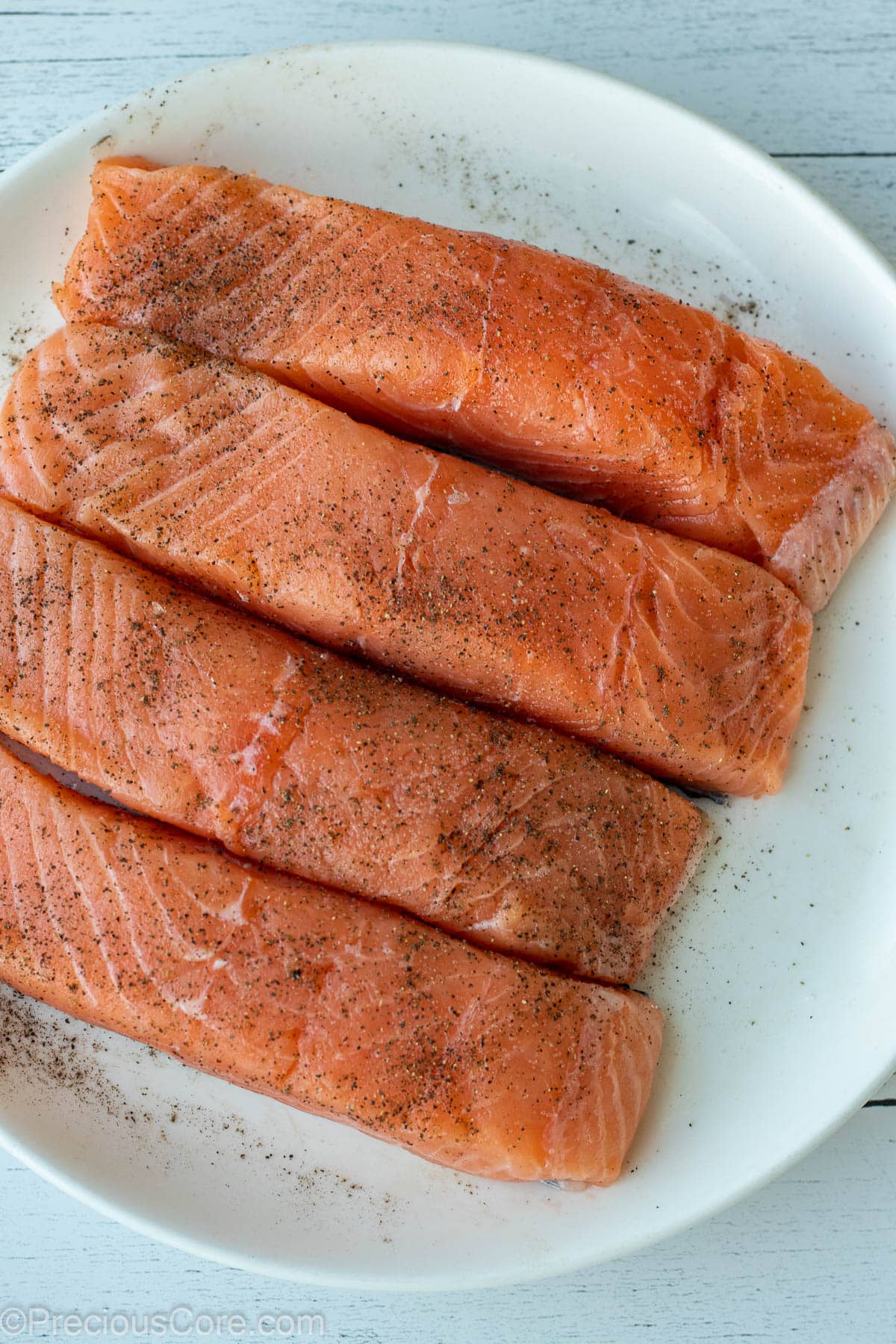 4 salmon fillet on a white plate, seasoned with salt and pepper.