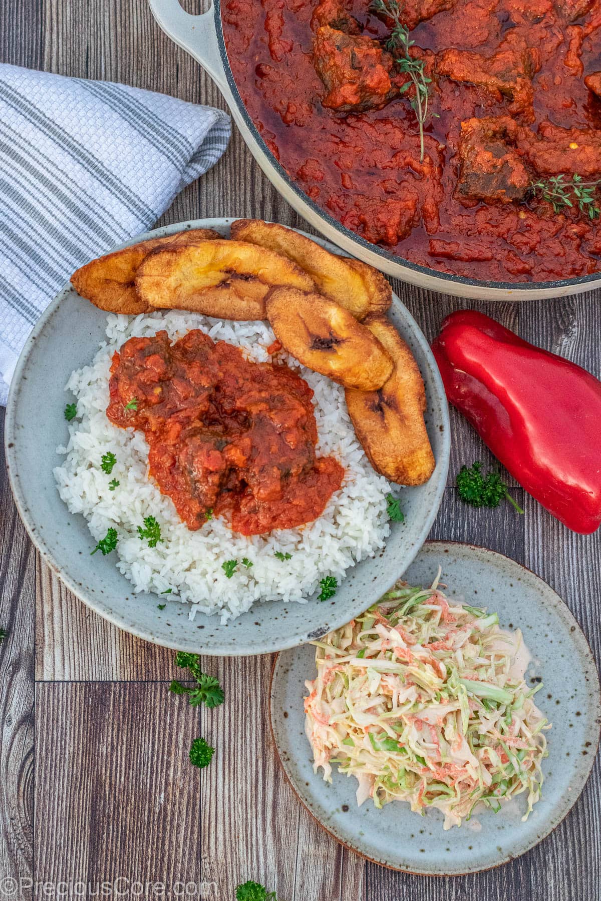 Nigerian beef stew served with rice and a side of sweet fried plantains and coleslaw.