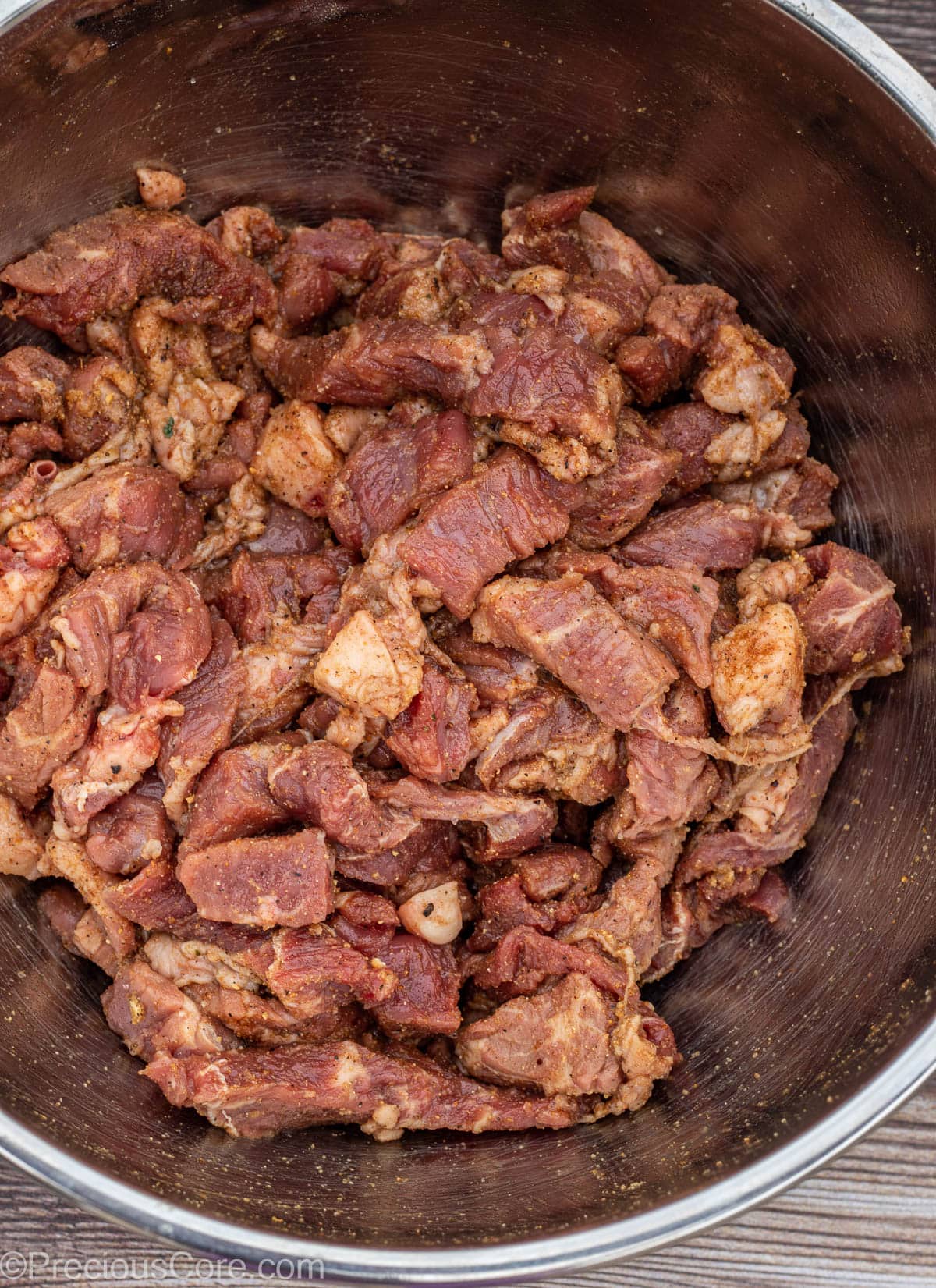 Seasoned bite-sized pieces of beef in a stainless steel bowl.