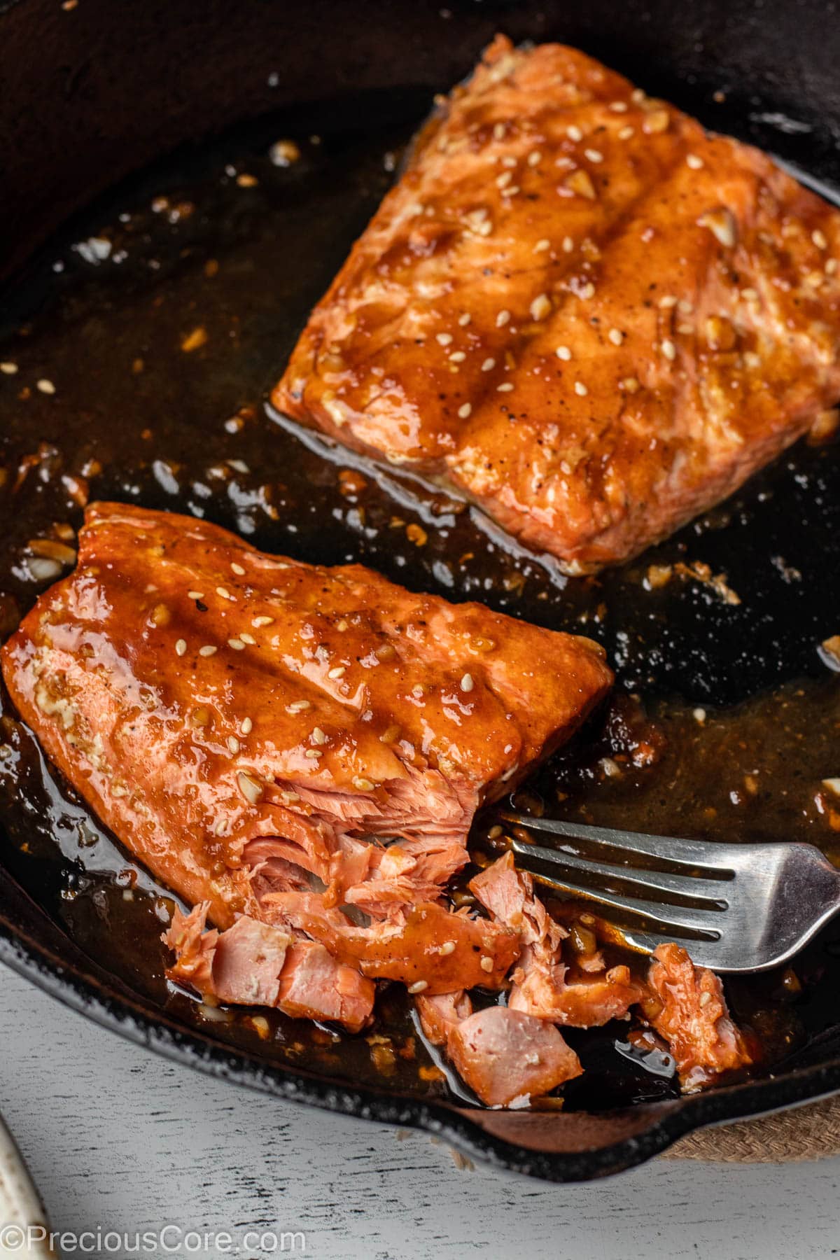 2 salmon fillets in a pan with some of the salmon flaked with a fork.